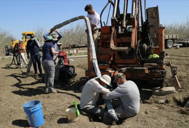 Seven people in an unplanted field collect data.