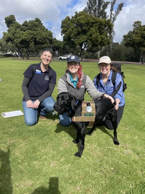 Three people smiling and posing with a detector dog