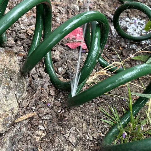 A garden hose with a hole in the middle of it and water is spraying out of the hole